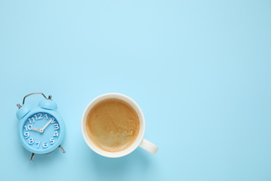 Photo of Cup of morning coffee and alarm clock on light blue background, flat lay. Space for text