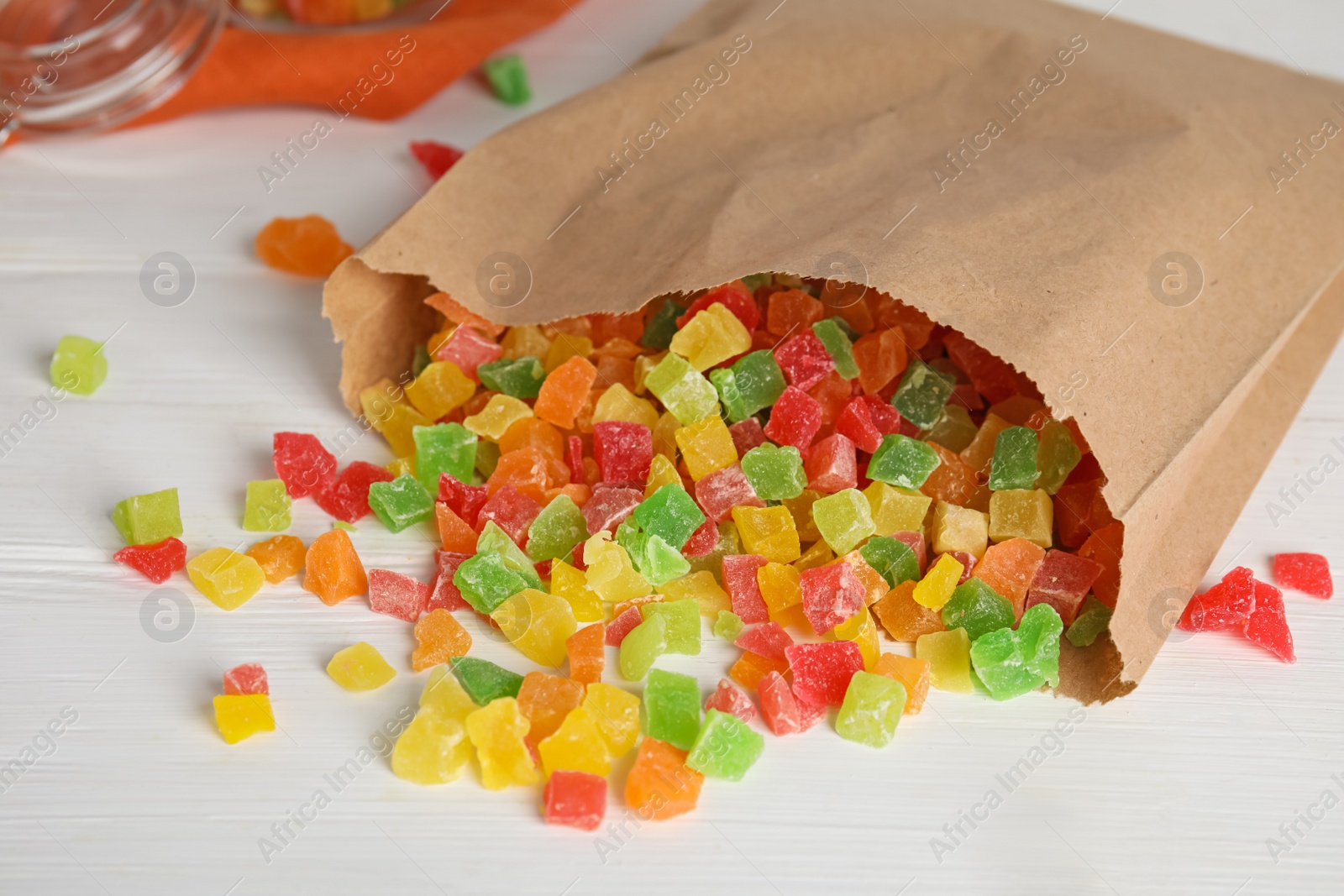 Photo of Overturned paper bag with mix of delicious candied fruits on white wooden table, closeup