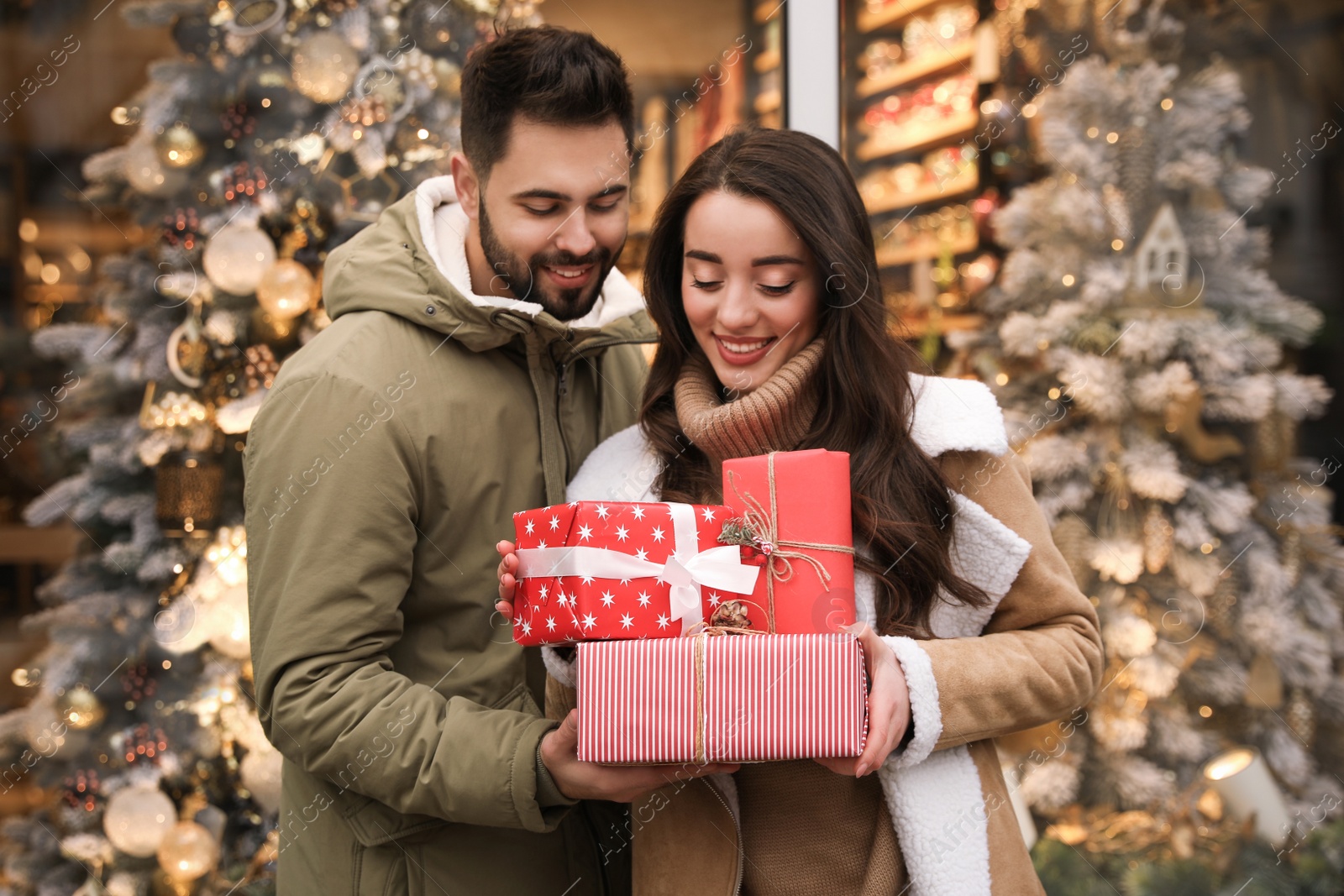 Photo of Lovely couple with presents near store decorated for Christmas outdoors