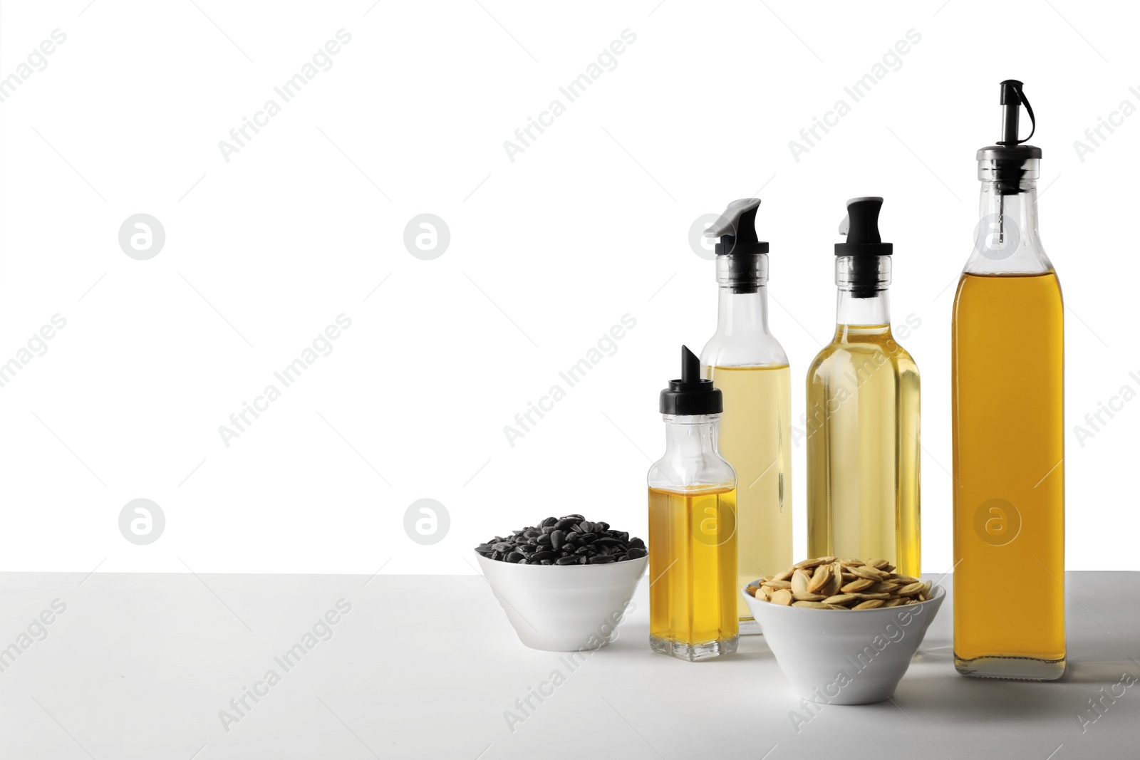 Photo of Bottles of different cooking oils and seeds on white background, space for text