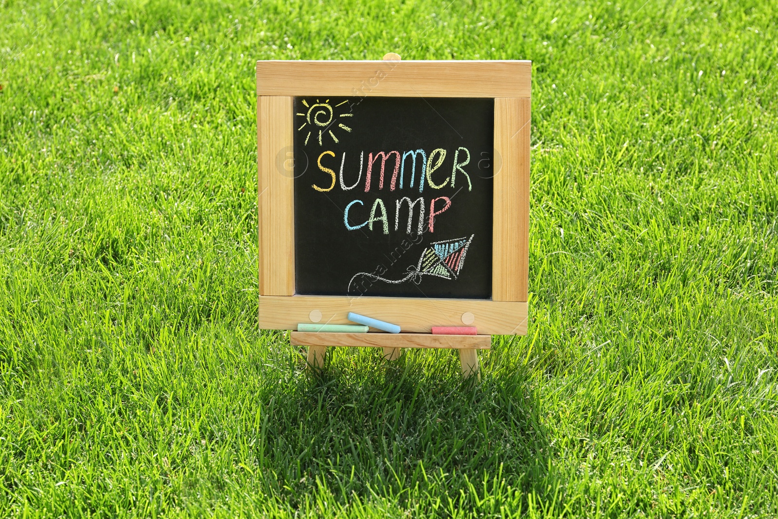 Photo of Blackboard with text SUMMER CAMP and drawings on green grass