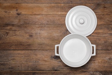 Photo of Empty white pot and lid on wooden table, flat lay. Space for text