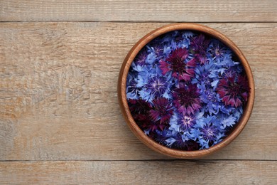 Photo of Beautiful colorful cornflowers in bowl on wooden table, top view. Space for text