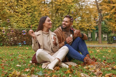 Photo of Happy young couple blowing soap bubbles in autumn park
