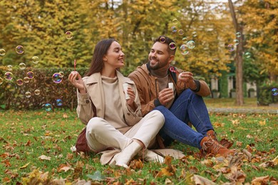 Happy young couple blowing soap bubbles in autumn park