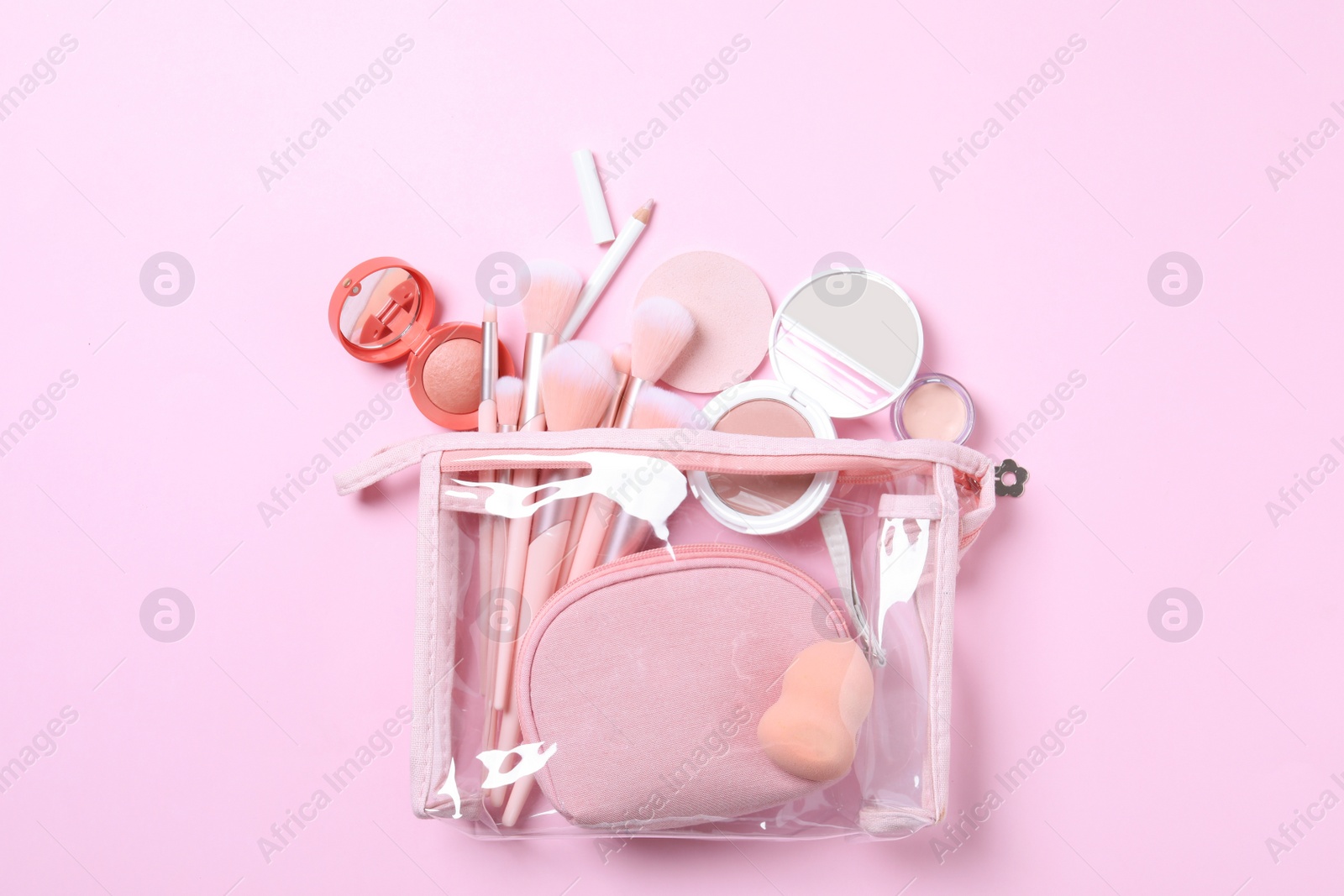 Photo of Plastic cosmetic bag with makeup products and beauty accessories on pink background, flat lay