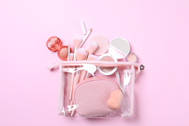 Photo of Plastic cosmetic bag with makeup products and beauty accessories on pink background, flat lay