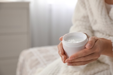 Photo of Woman with jar of moisturizing cream indoors, closeup