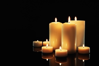 Photo of Different wax candles burning on table in darkness