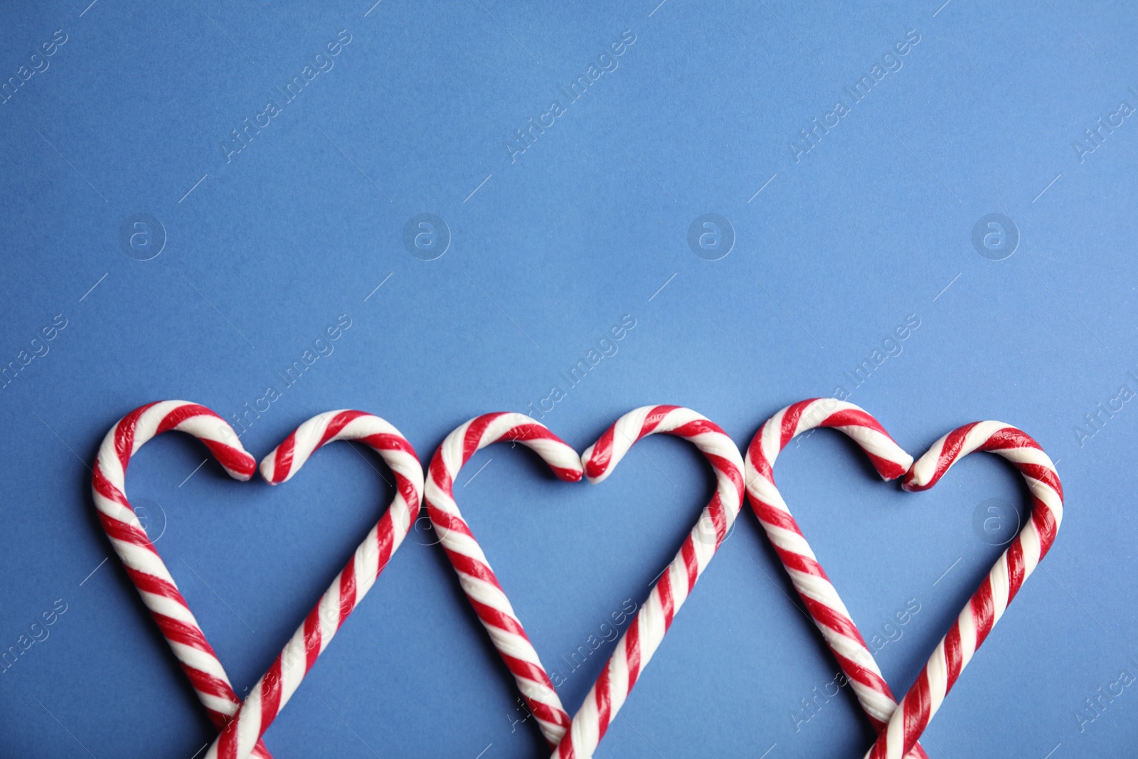 Photo of Candy canes on blue background, flat lay. Space for text