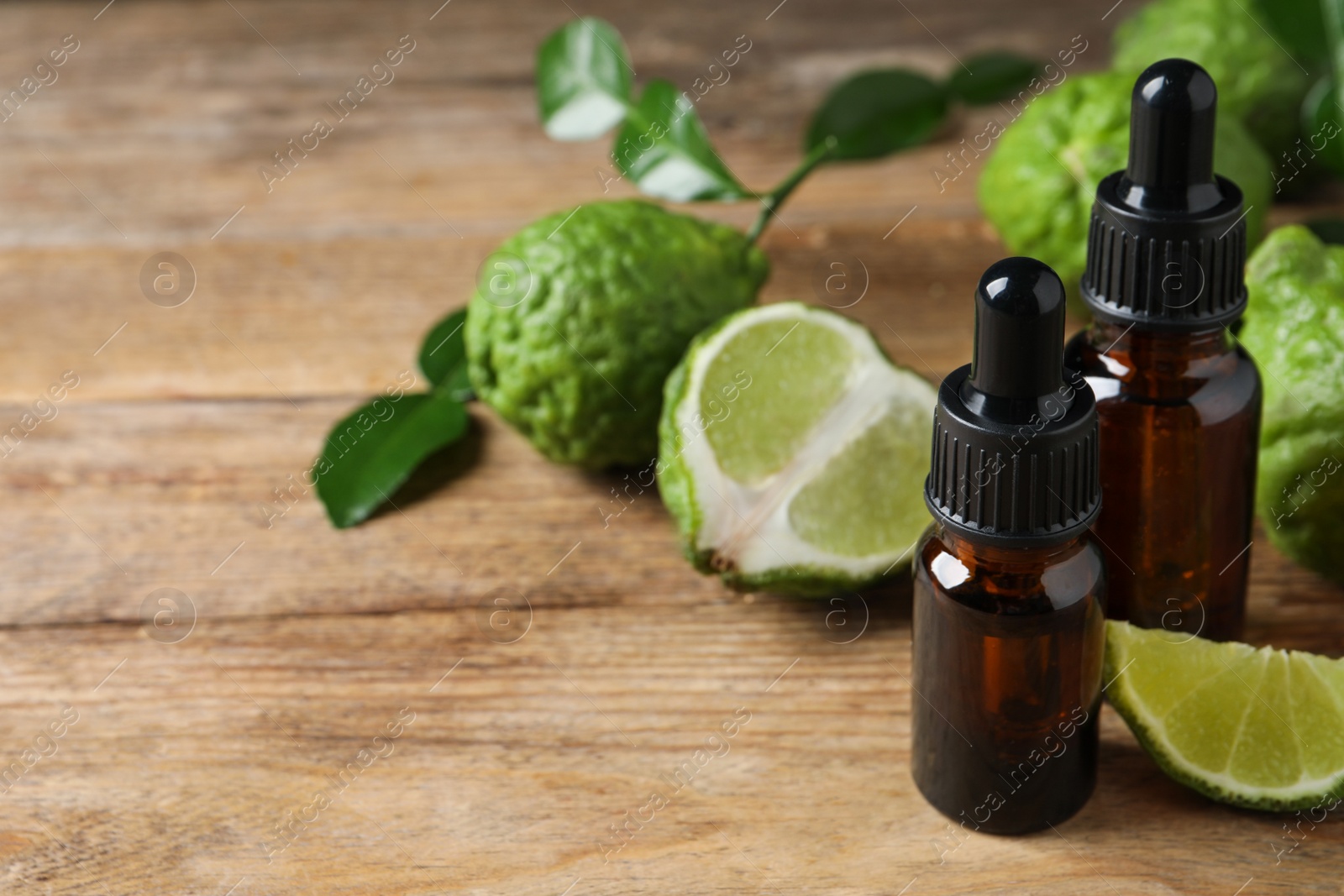 Photo of Bottles of essential oil and fresh bergamot fruits on wooden table. Space for text