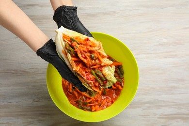 Woman preparing spicy cabbage kimchi at wooden table, top view
