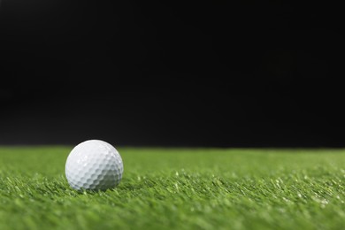 Photo of Golf ball on green grass against black background, space for text