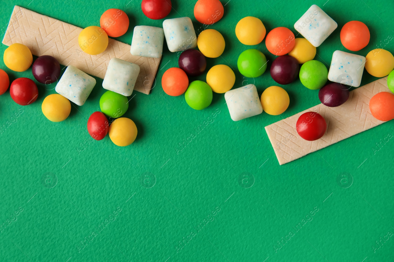 Photo of Different tasty chewing gums on green background, flat lay. Space for text