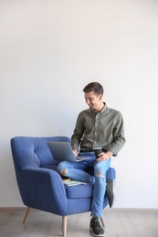 Photo of Young blogger with laptop sitting on armchair against light wall