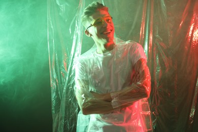 Stylish young man wearing clear coat and glasses in neon lights