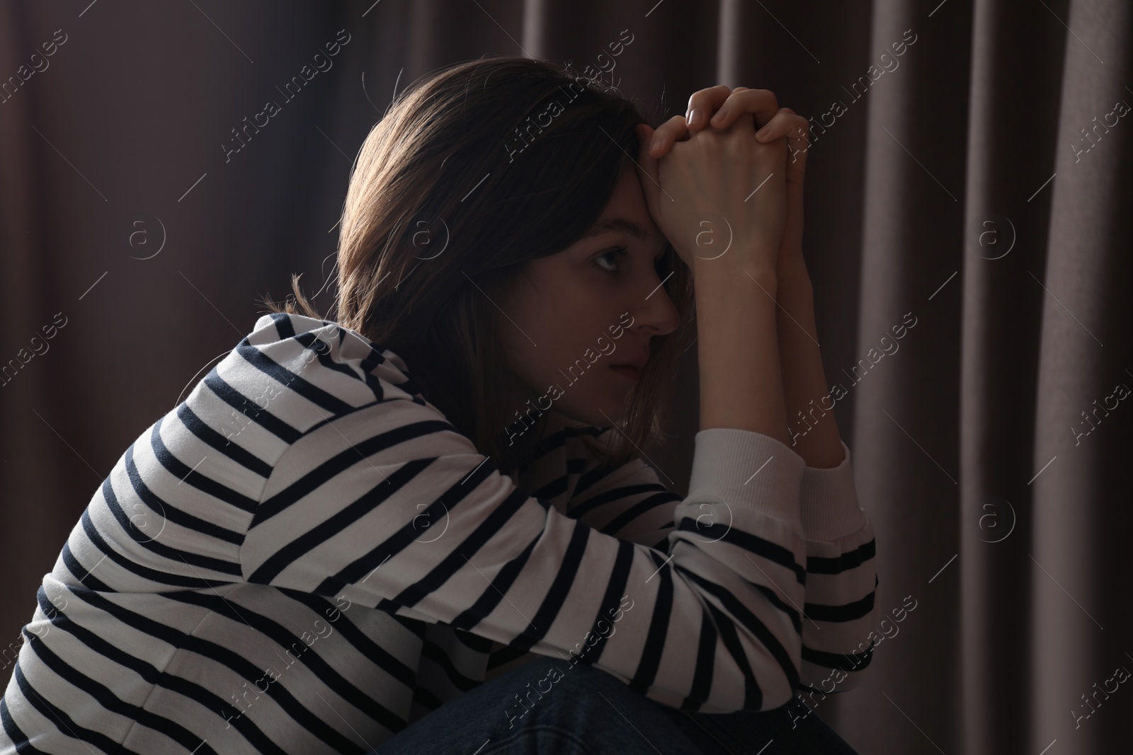 Photo of Sad young woman near closed curtains indoors