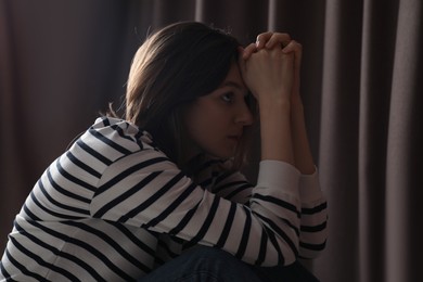 Sad young woman near closed curtains indoors