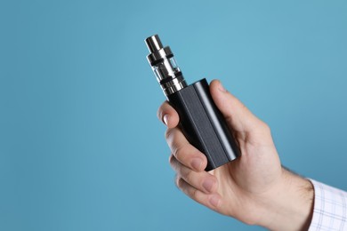 Man holding electronic cigarette on light blue background, closeup