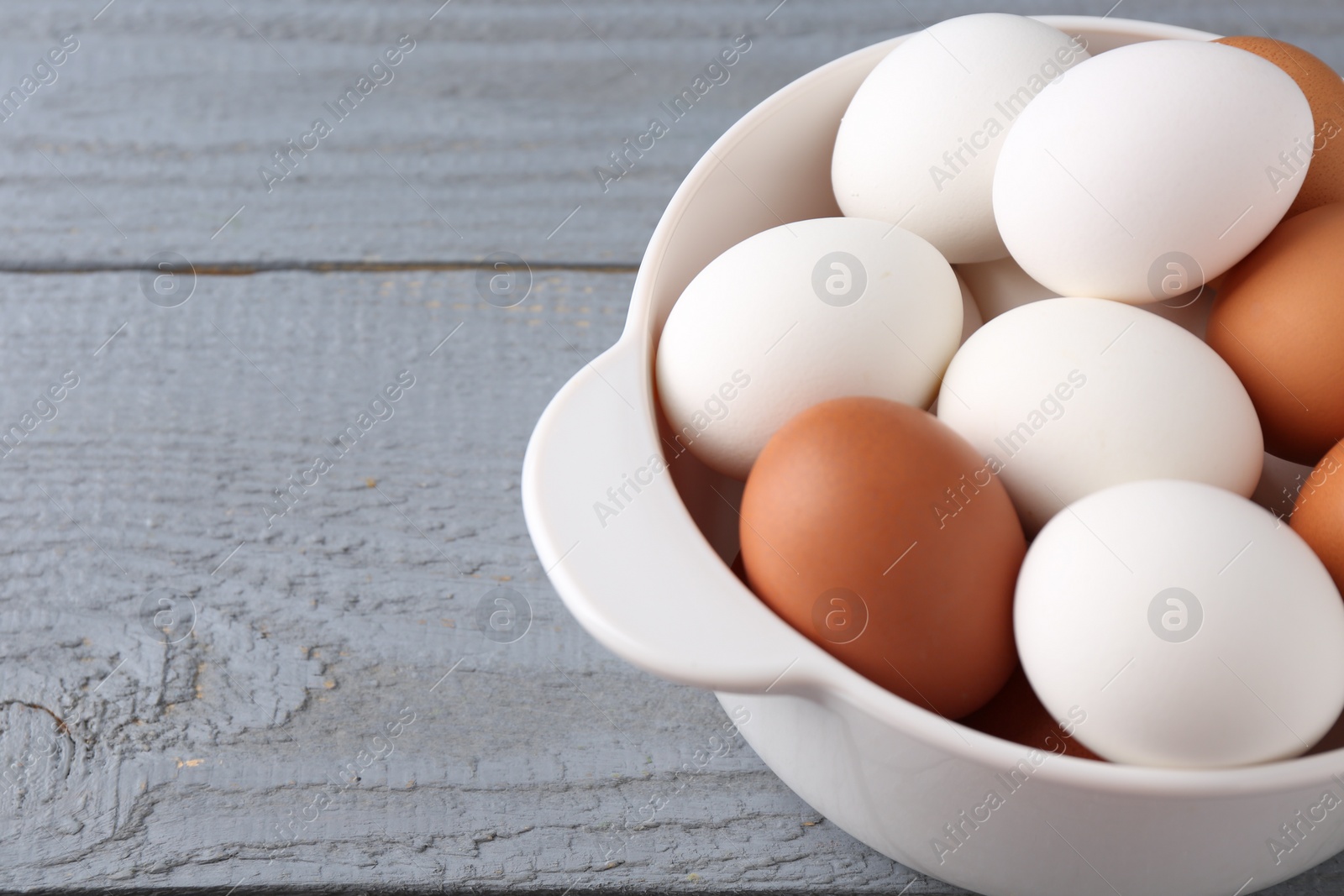 Photo of Unpeeled boiled eggs in saucepan on grey wooden table, closeup. Space for text