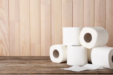 Photo of Rolls of toilet paper on wooden table. Space for text