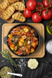 Photo of Dish with tasty ratatouille, ingredients and bread on black table, flat lay