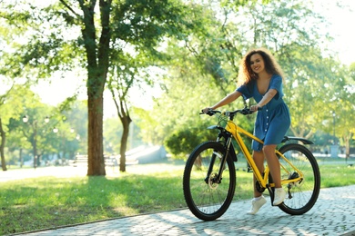 Beautiful young African-American woman with bicycle in city park