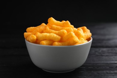 Photo of Bowl with crunchy cheesy corn snack on black wooden table, closeup
