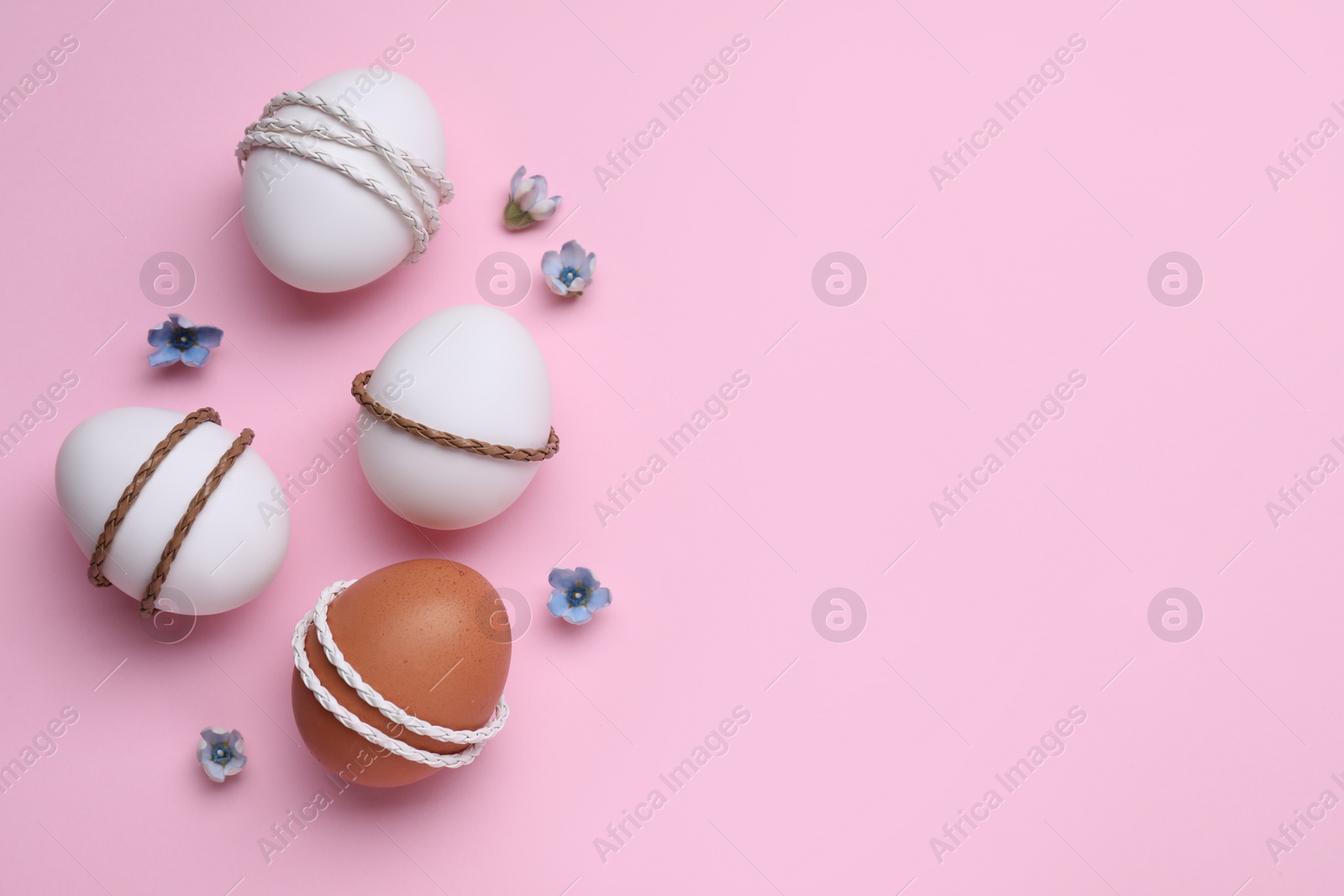 Photo of Beautifully decorated Easter eggs and flowers on pink background, flat lay. Space for text