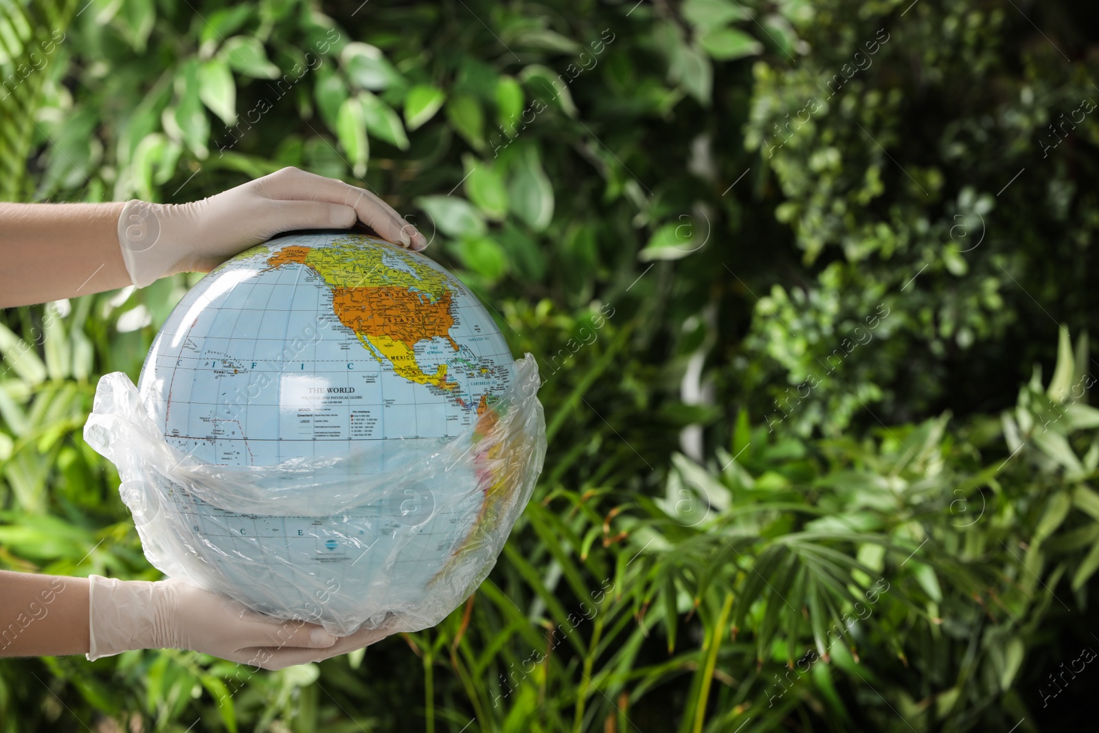 Photo of Woman holding globe in plastic bag against green leaves, closeup. Space for text. Environmental conservation