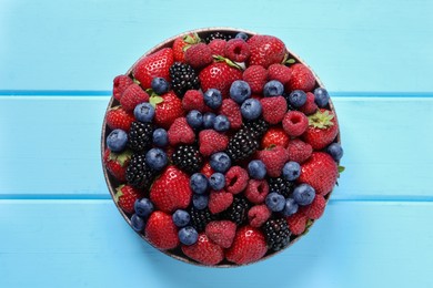 Different fresh ripe berries in bowl on light blue wooden table, top view