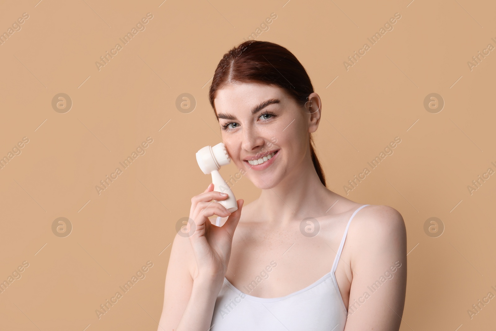 Photo of Washing face. Young woman with cleansing brush on beige background