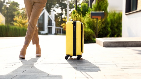 Photo of Young businesswoman with yellow suitcase outdoors. Moving day