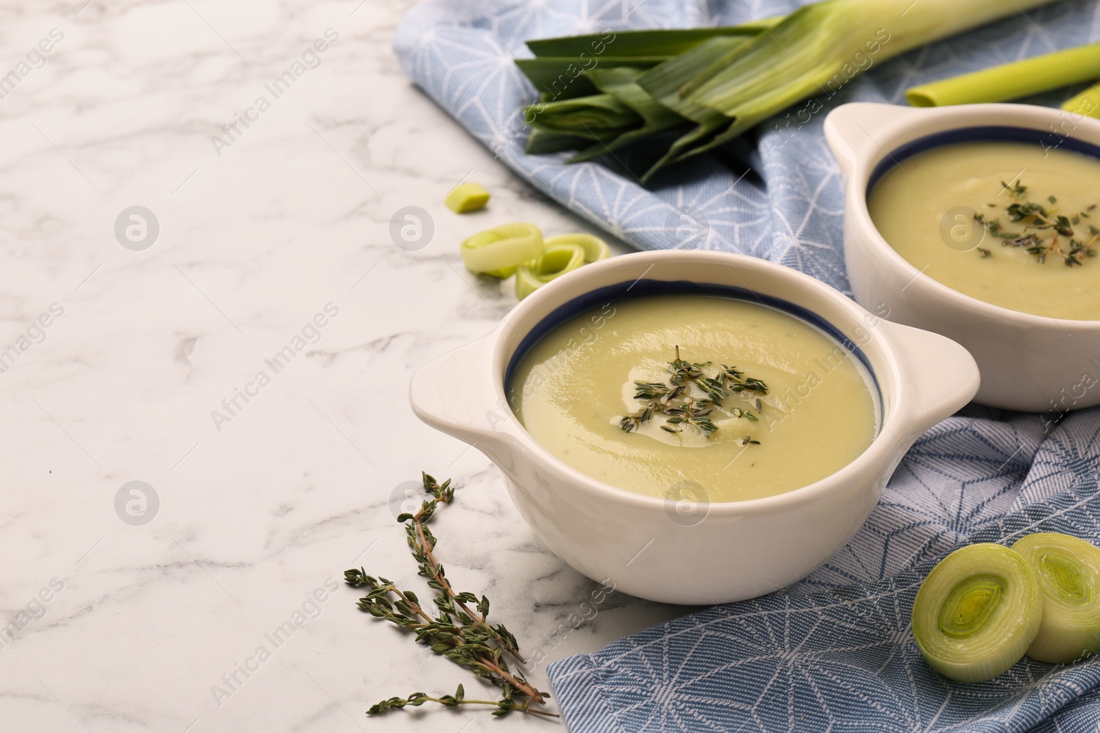 Photo of Tasty leek soup in bowls on white marble table, space for text