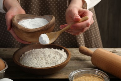 Making dough. Woman adding baking powder to flour at wooden table, closeup