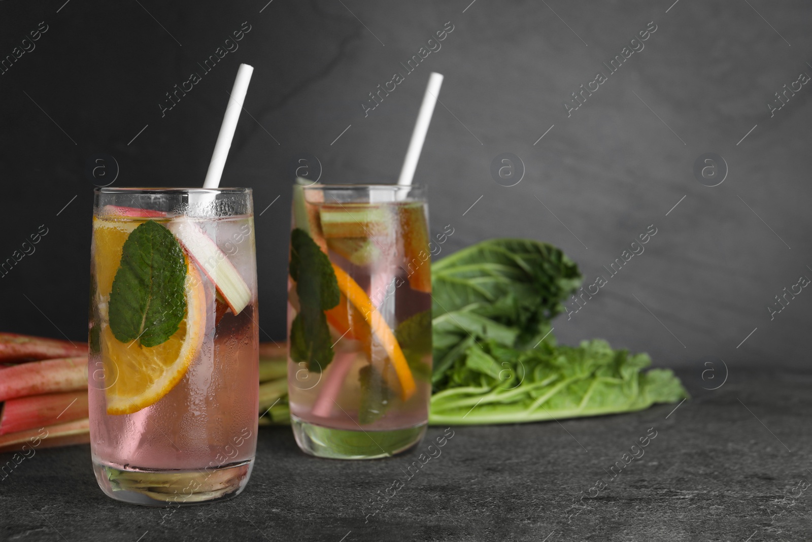 Photo of Tasty rhubarb cocktail with lemon on grey table, space for text