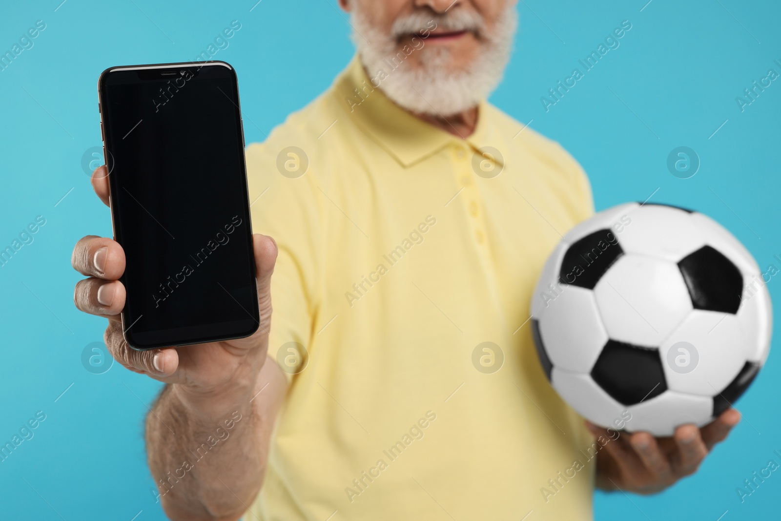 Photo of Sports fan with soccer ball showing smartphone on light blue background, closeup