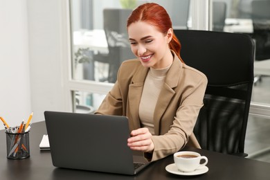 Happy woman working with laptop at black desk in office