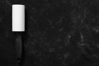 Photo of Lint roller and pet hair on black fabric, top view. Space for text