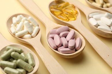 Different vitamin pills in spoons on pale yellow background, closeup