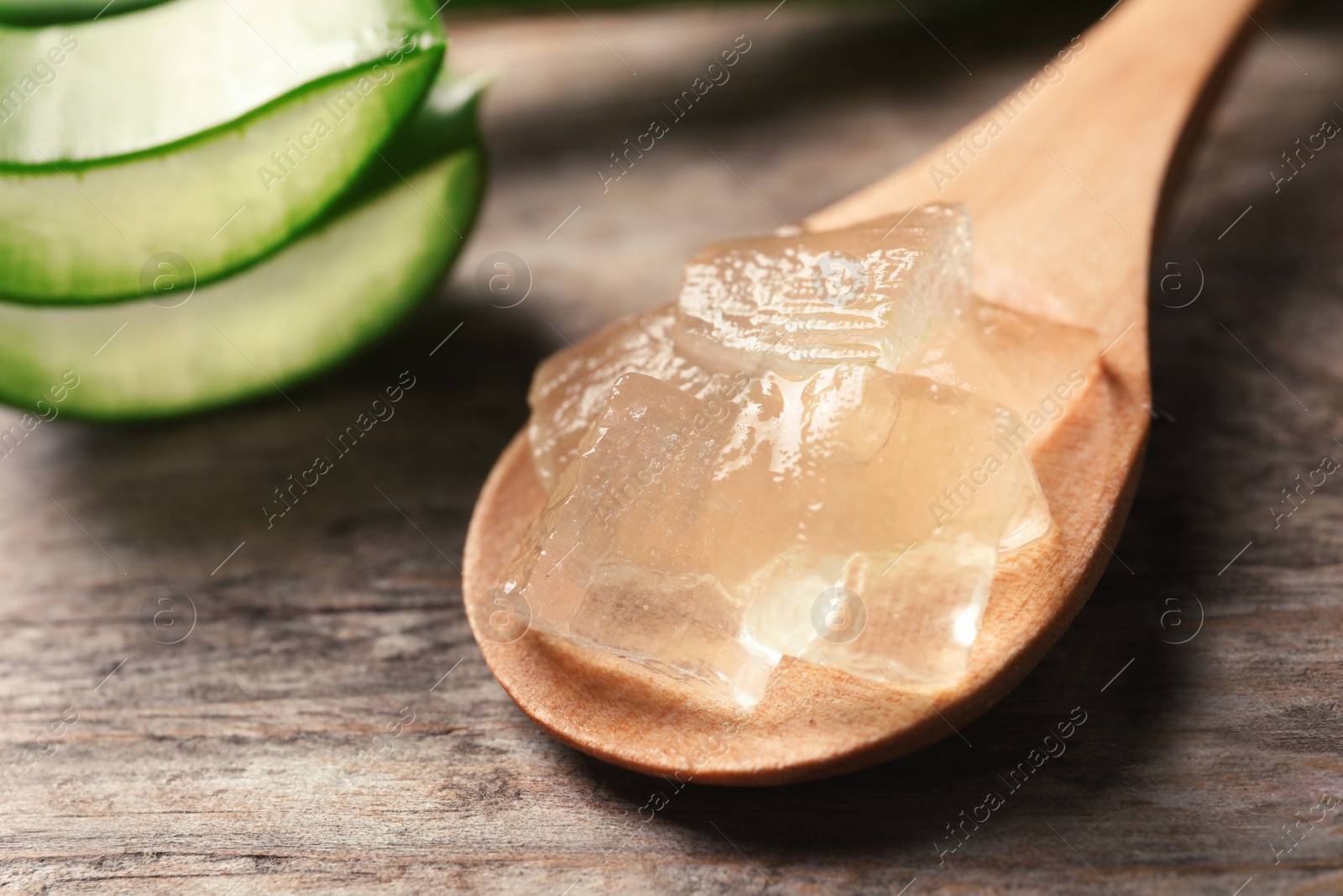 Photo of Spoon with aloe vera gel on wooden background, closeup