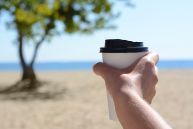 Woman with takeaway coffee cup on beach, closeup. Space for text