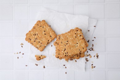 Photo of Cereal crackers with flax and sesame seeds on white tiled table, top view