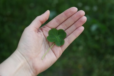 Photo of Woman holding one beautiful green clover leaf outdoors, closeup