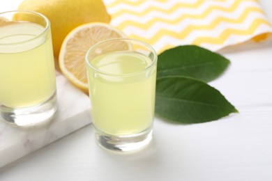 Photo of Tasty limoncello liqueur, lemons and green leaves on white table, closeup. Space for text