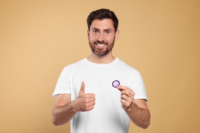 Photo of Happy man with condom showing thumb up on beige background. Safe sex