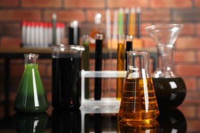 Laboratory glassware with different types of oil on black mirror table indoors, closeup