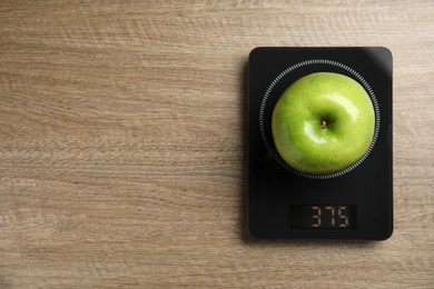 Photo of Ripe green apple and electronic scales on wooden table, top view. Space for text