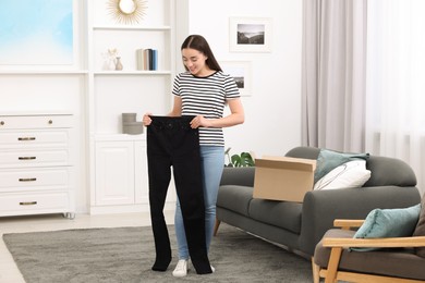 Photo of Happy woman with stylish black jeans at home. Online shopping