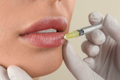 Woman getting lip injection on beige background, closeup